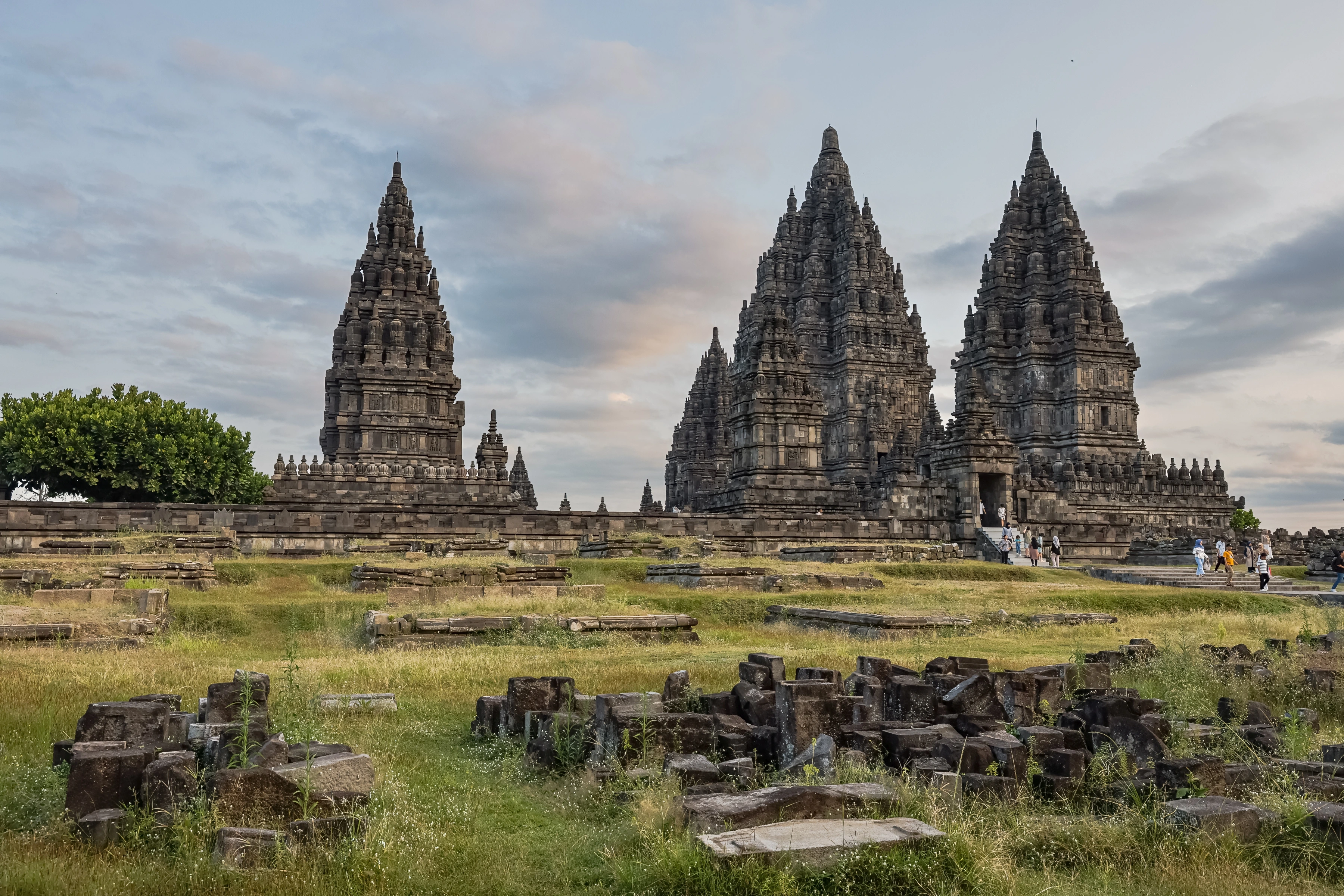 Tall stone temple towers rise beyond scattered blocks and visitors.