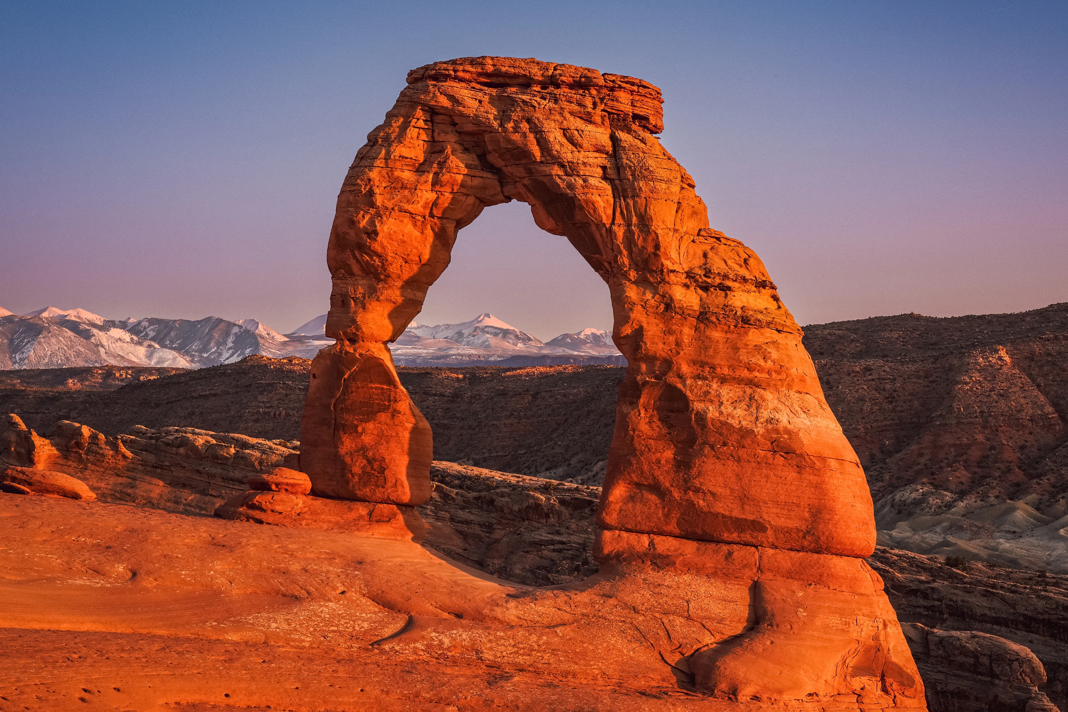 An orange sandstone arch frames distant snow-covered mountains.