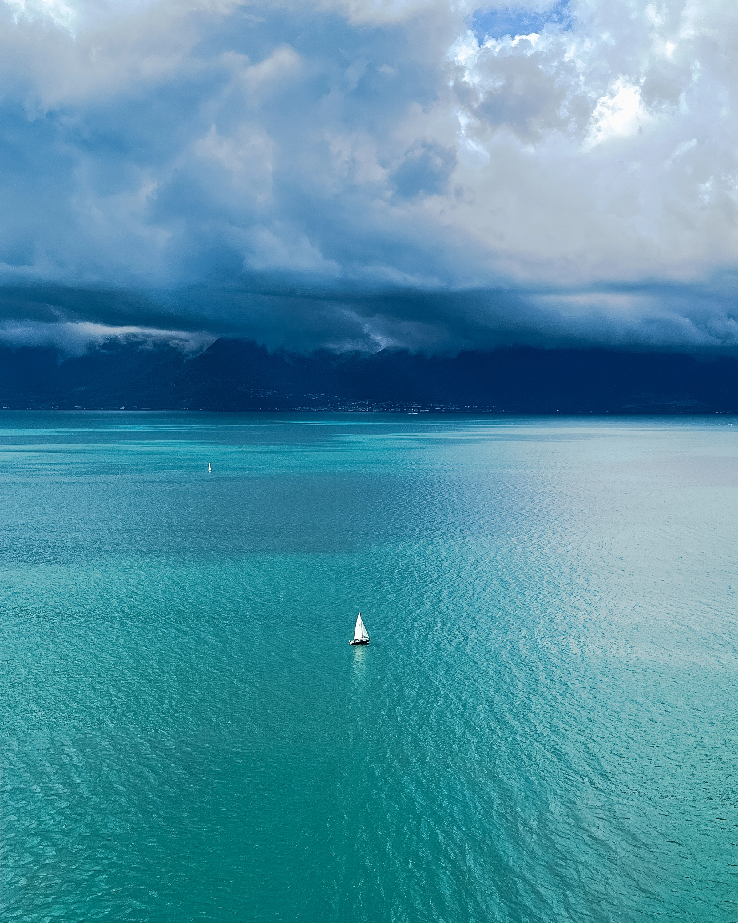 Small sails sit beneath a low cloud ceiling over a turquoise lake.