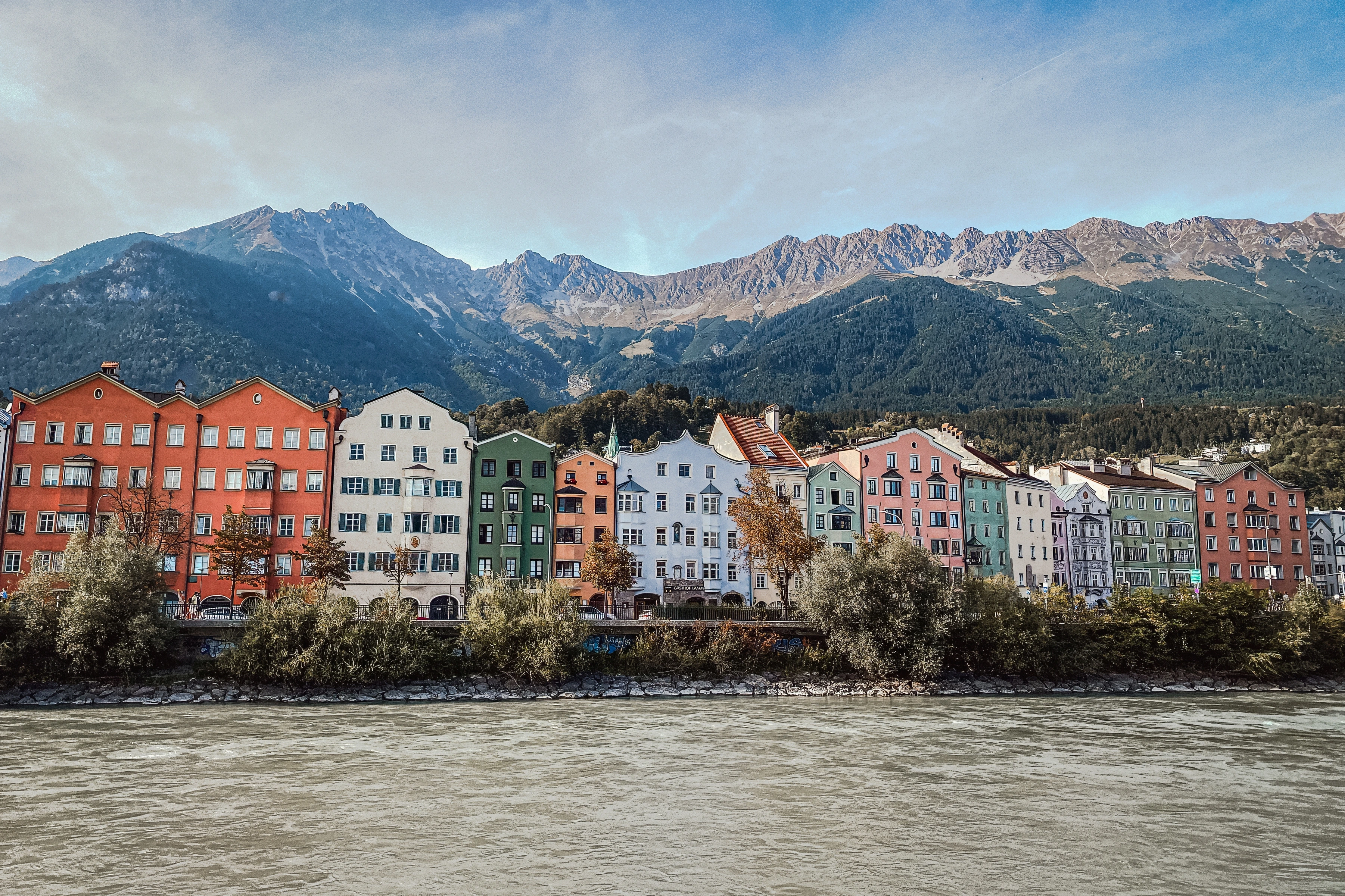 A row of colourful gabled buildings borders a river, with a mountain ridge rising behind.