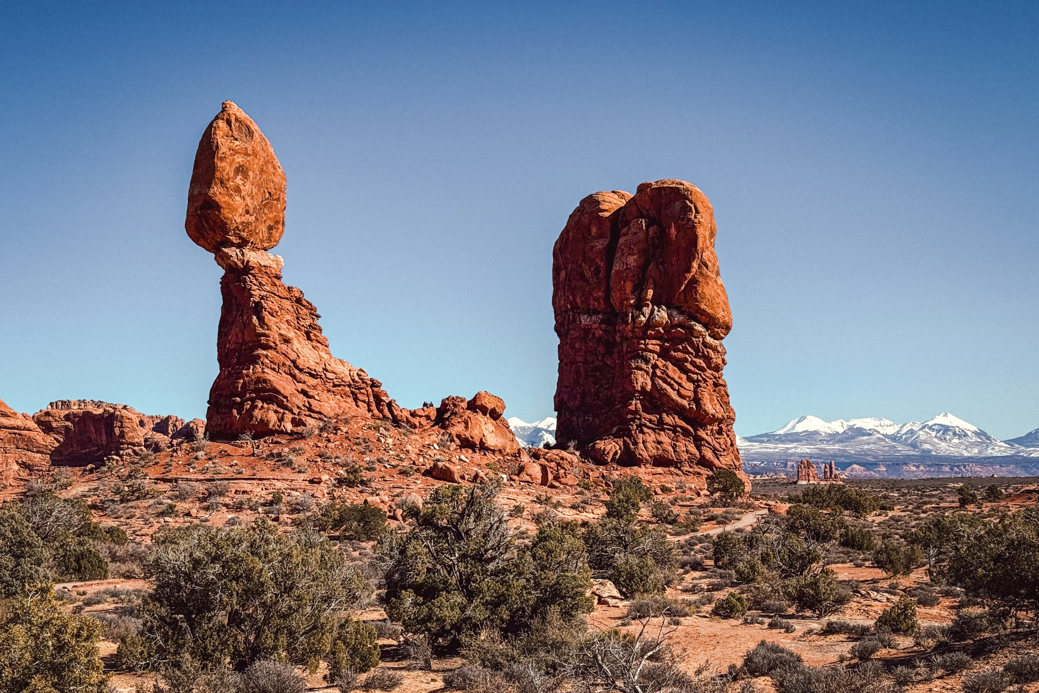Large rounded and columnar rock forms stand above scrub, with a pale snowy ridge in the distance.