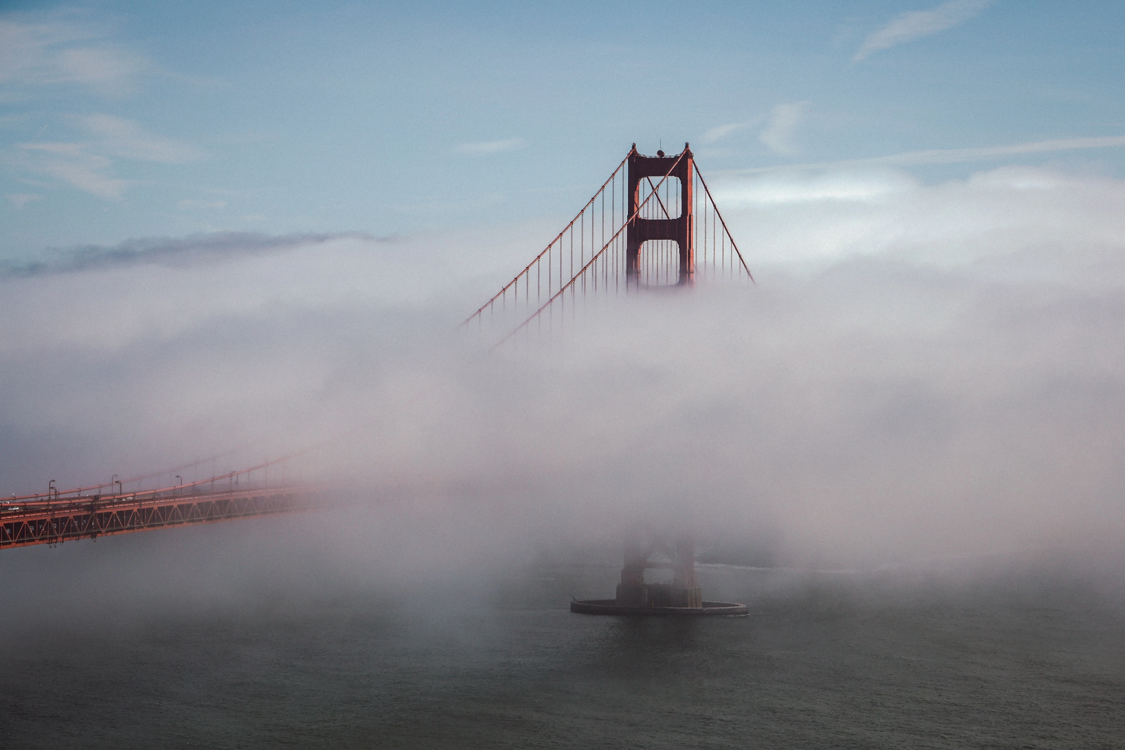 A suspension-bridge tower and road emerge from broad coastal fog.