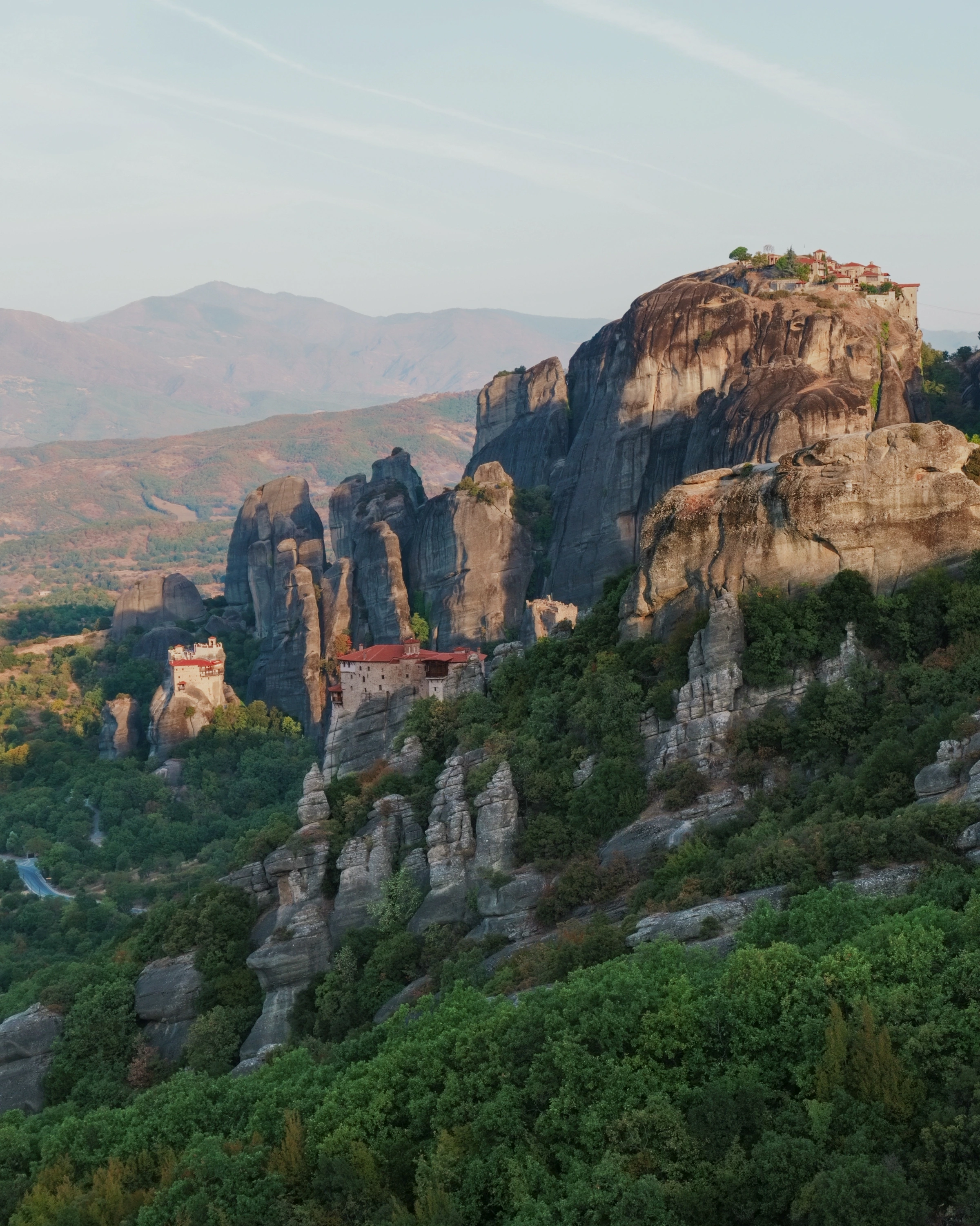 Buildings sit among tall rock pillars above wooded slopes.