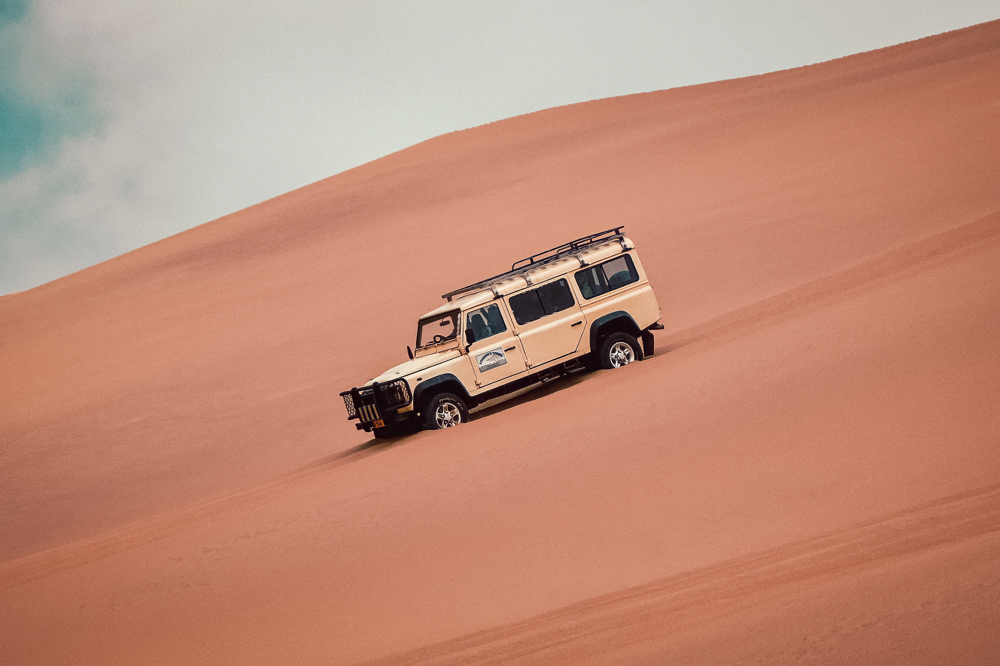 A white vehicle crosses a steep orange dune marked by tracks.