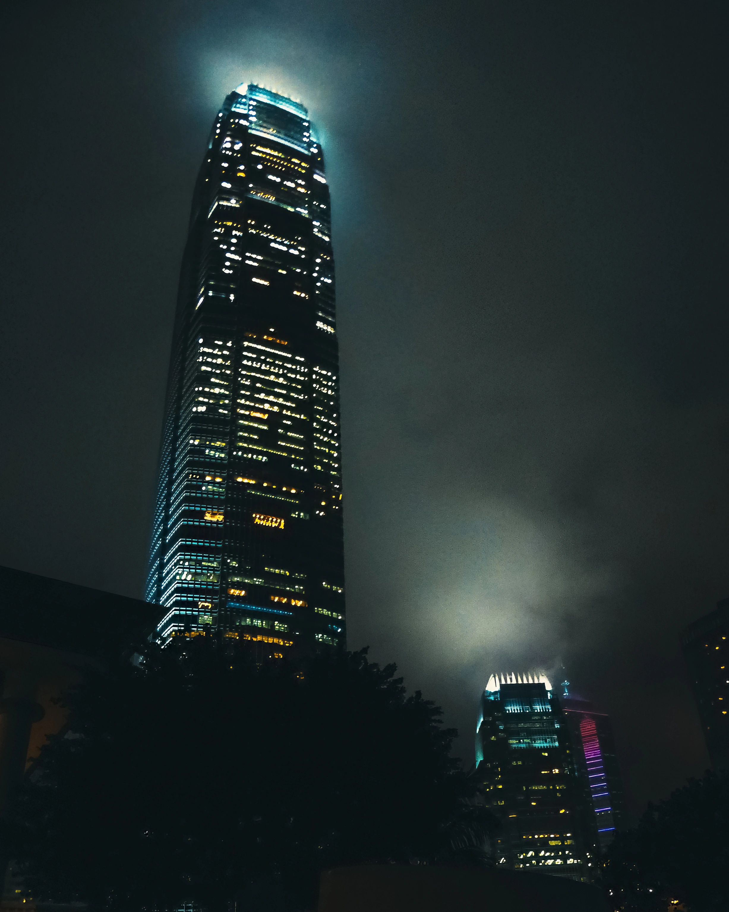Lit towers rise through dark haze, with one tall building dominating the left side.