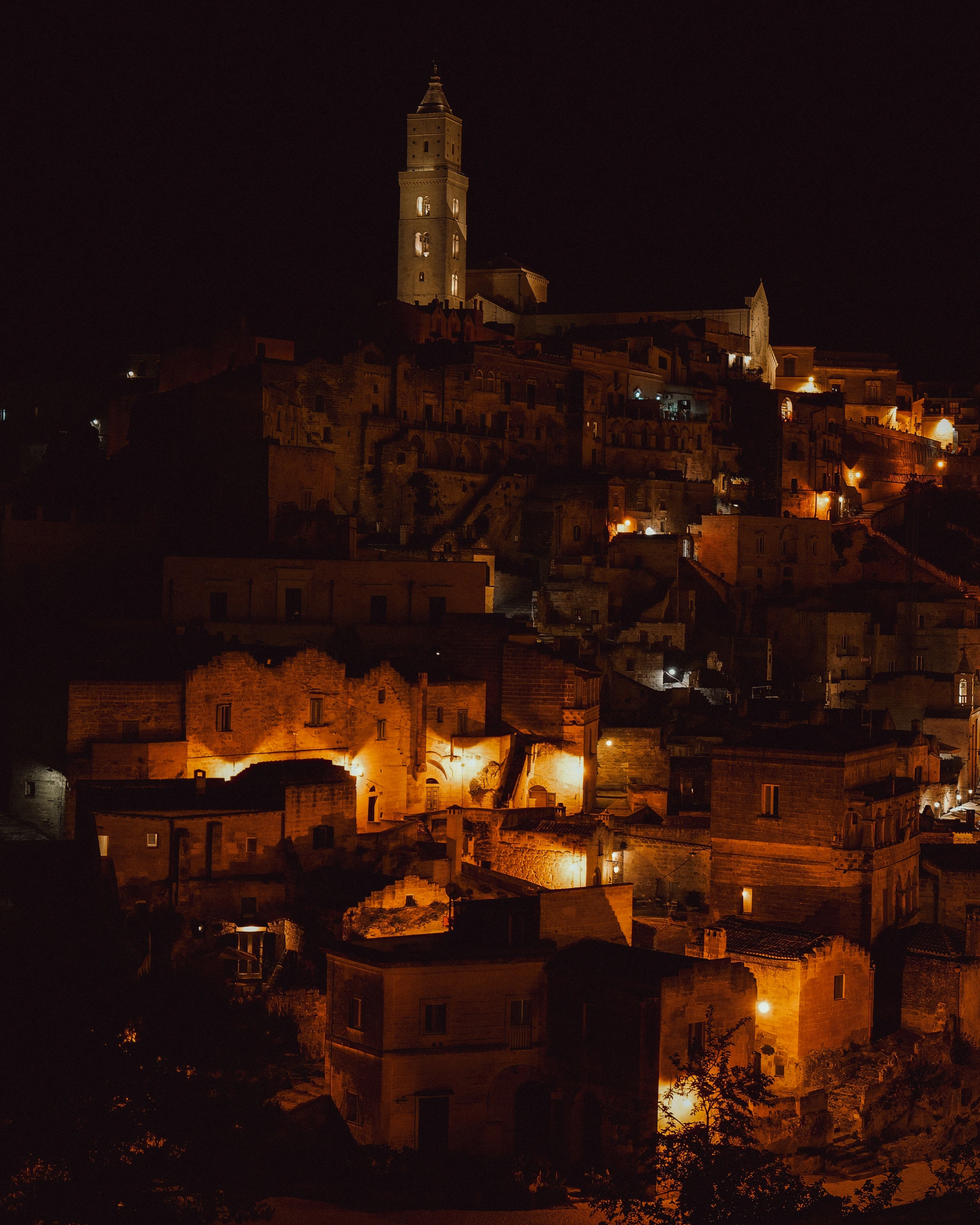 Warm pools of light reveal stacked stone buildings below a tall bell tower.