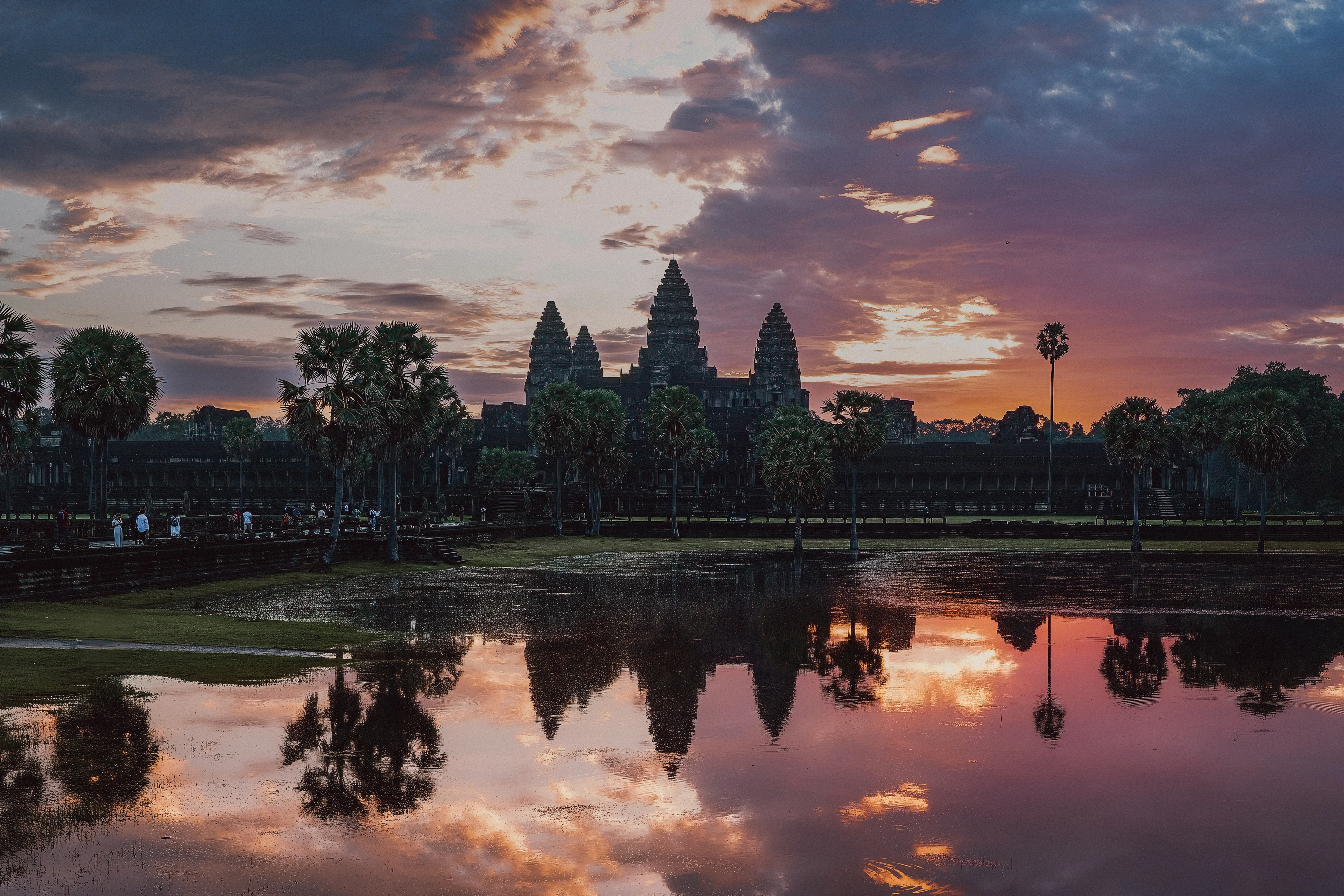 Temple towers and palms reflected in a pool beneath coloured dawn clouds.